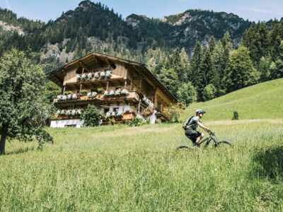 Mountainbiker in Alpbach vorbei an den urigen Bauernhäusern mit dem wunderschönen Blumenschmuck an den Balkonen © Alpbachtal Tourismus